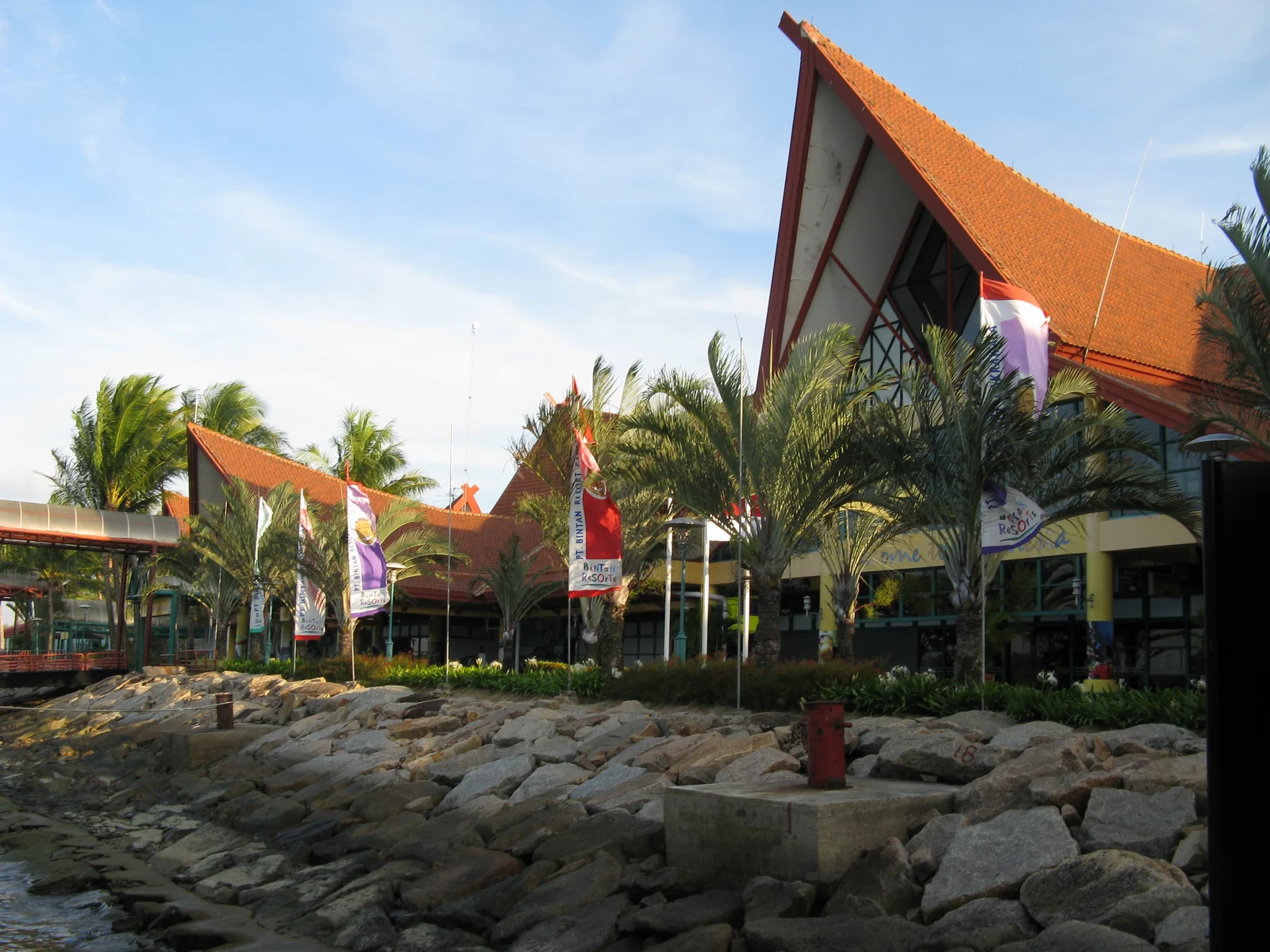 Bangunan terminal Bandar Bentan Telani dengan atap berwarna jingga dan deretan pohon kelapa